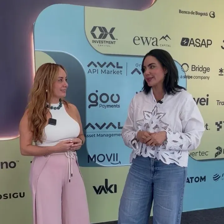 Conversación entre dos mujeres frente a los stands de Aval, Movii y Vaki